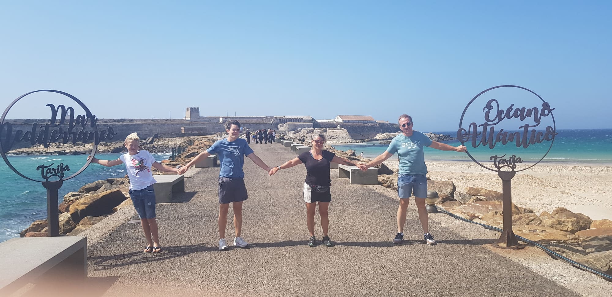 Famille se tenant la main entre la Méditerranée et l’Atlantique à Tarifa, symbole de lien, d’équilibre et de transparence – valeurs de Coco Swap